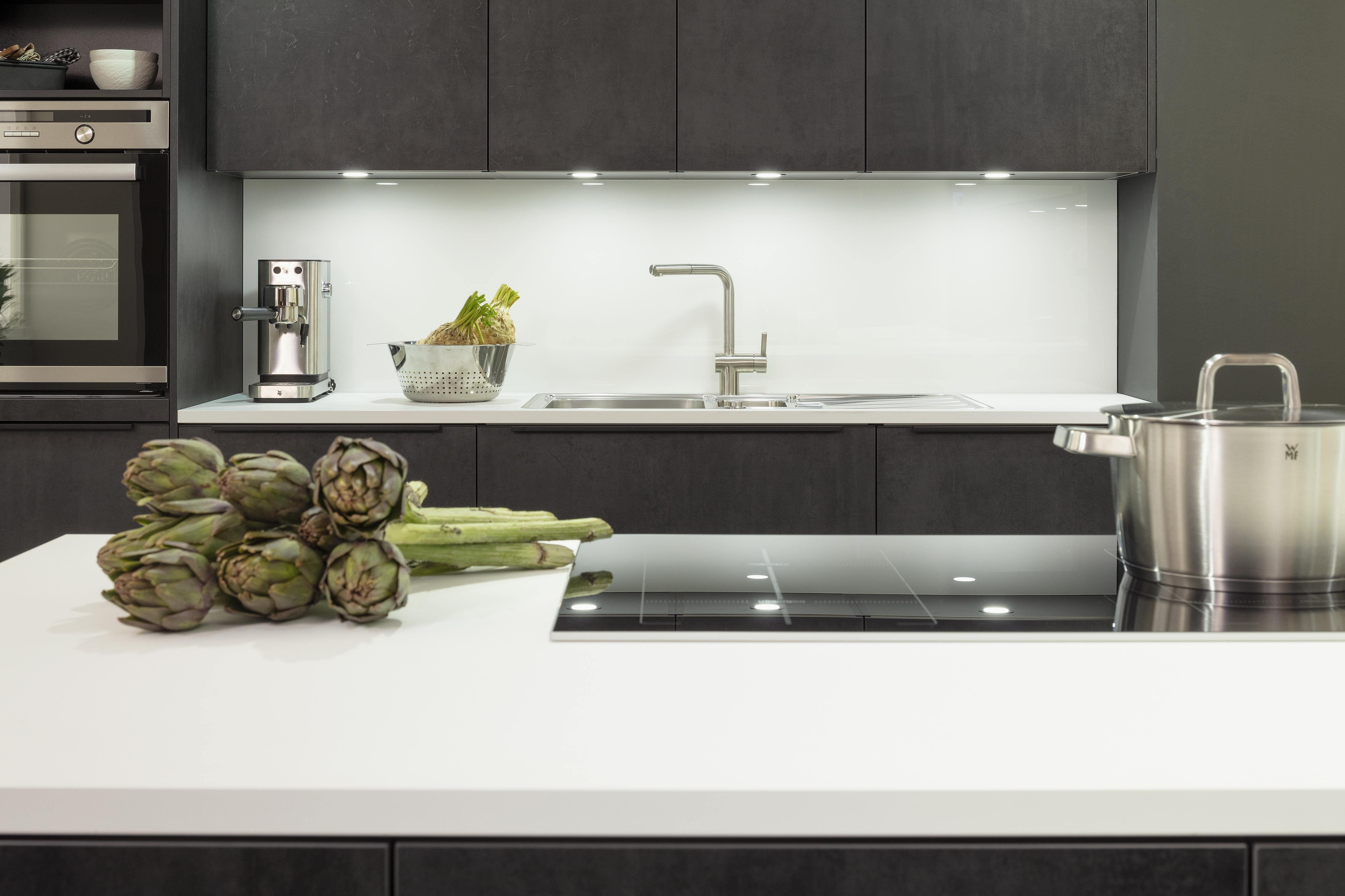 Beleuchtete Nische mit Spüle und Kochfeld im Vordergrund. 