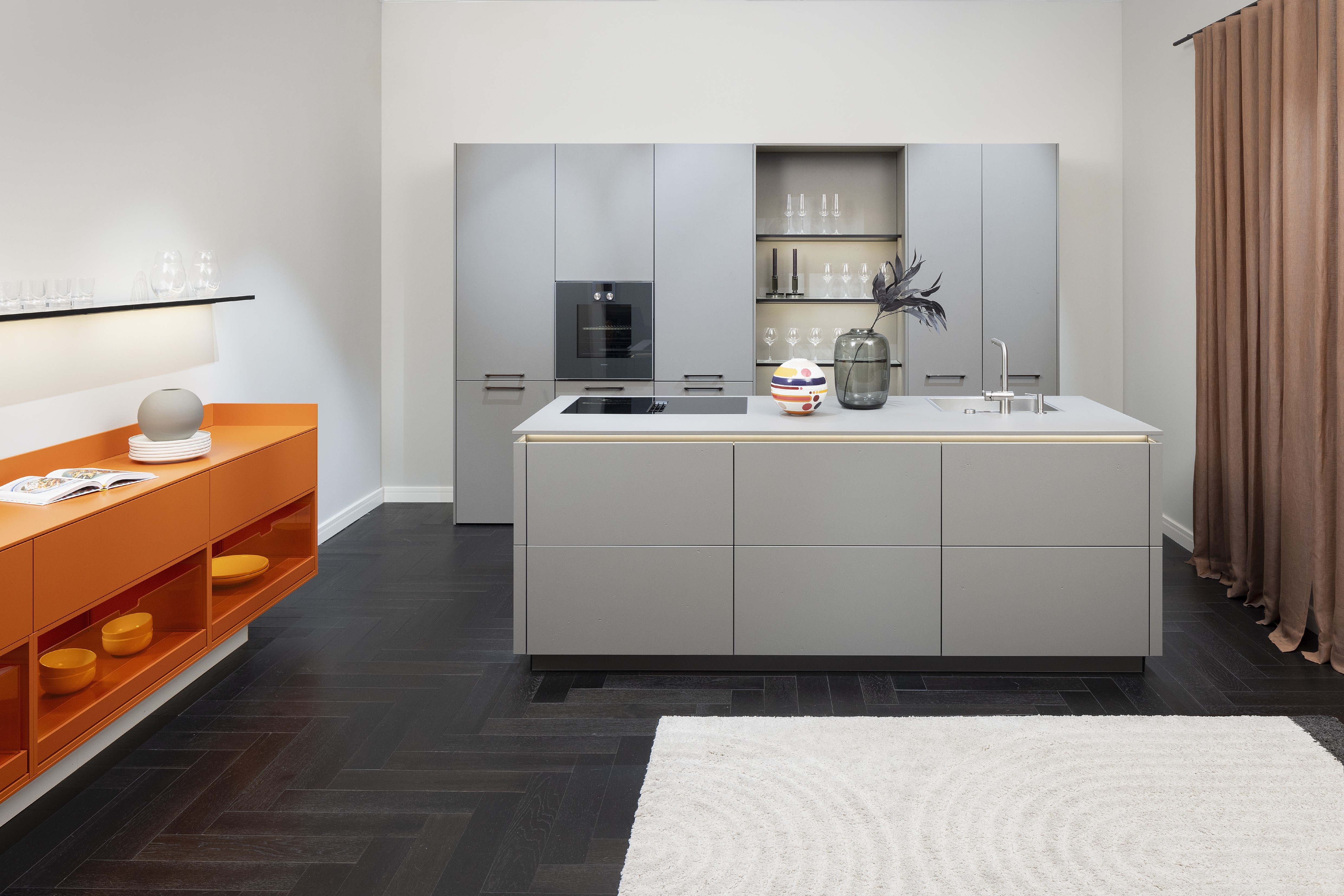 APL: 171 Greige 16 mm Front: AV 7010-GL Beton-grau, mineralischer Spachtelbeton (PUResist, PURemmision) Front Lack Orange Korpus: 2059 Designkorpus Titan Griff: Metall Black Chrome und Kehlleiste 359 Greige matt Kehlleiste Graphit gebürstet Geräte: Gaggenau Armatur: Franke Spüle: Franke  Features: Betonoberfläche individuell nachbearbeitet, Nischenrückwand Regal Betonoberfläche, Sideboard Orange mit offenen Schubkästen in Plexiglas Orange exklusives Auszugssystem im Schrank für mehr Stauraum, Sideboard 