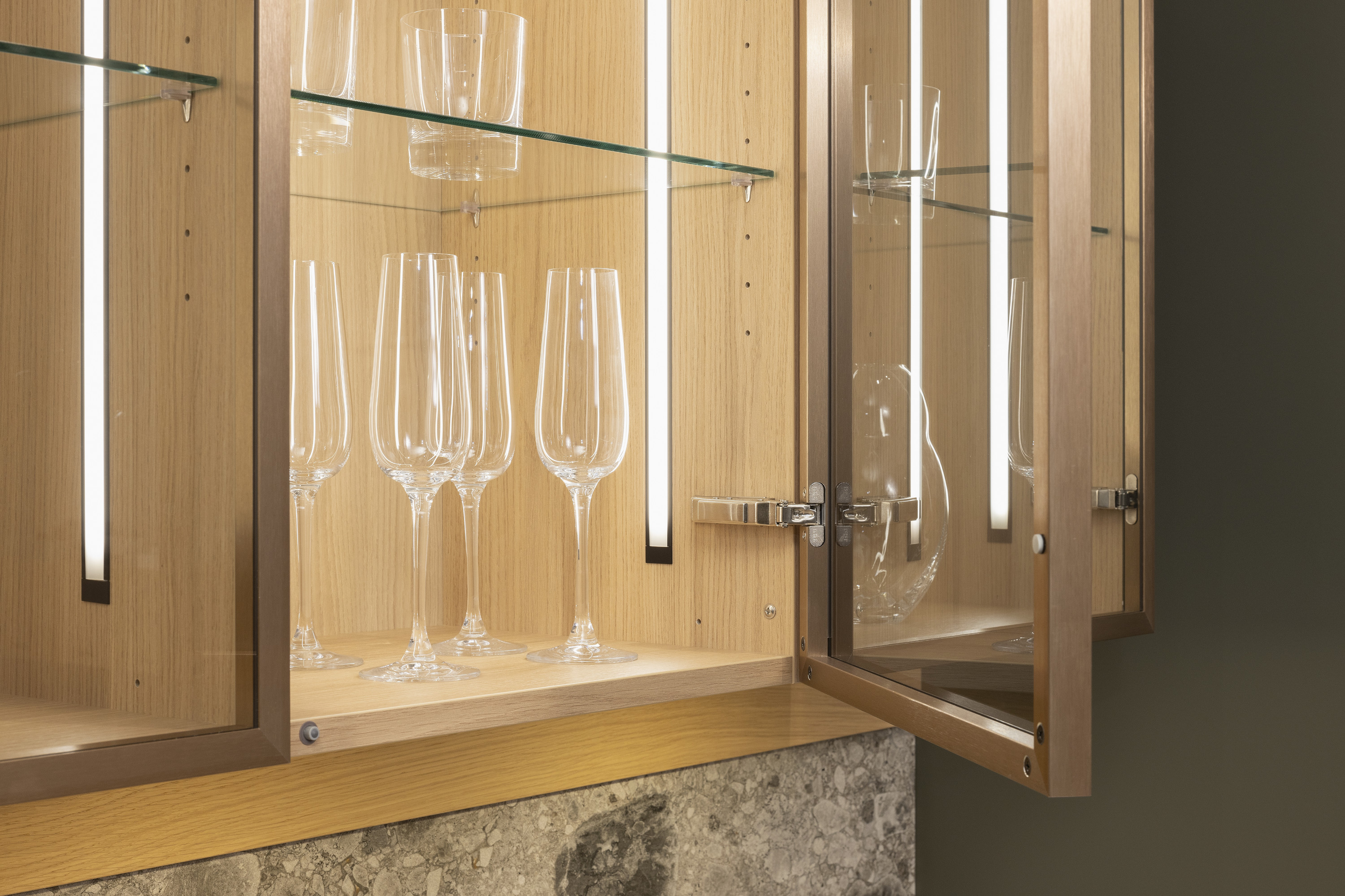 Geöffneter Holzschrank mit Glastüren und mehreren Weingläsern auf Glasboden.