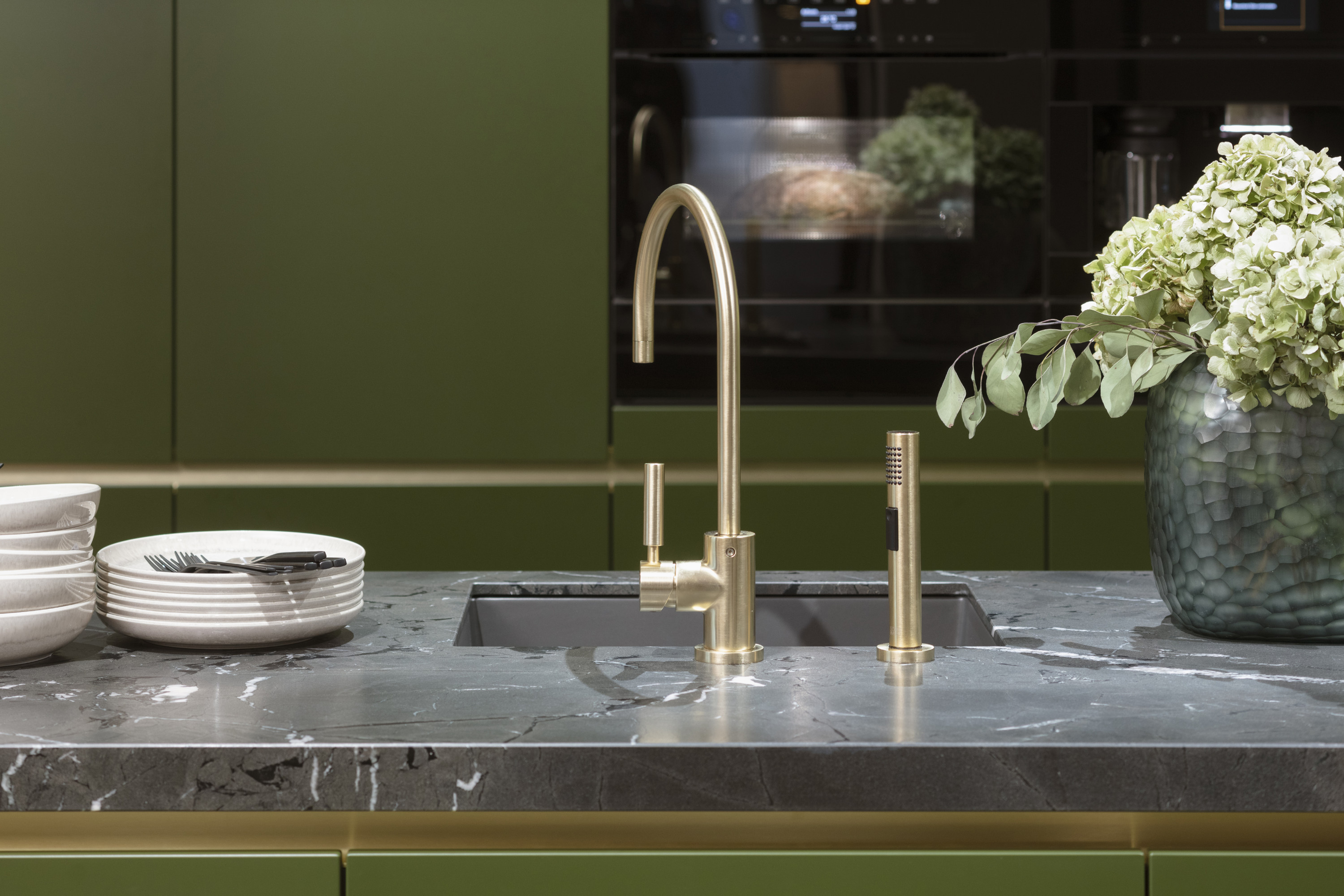 Moderne Küche mit Marmor-Arbeitsplatte, Messingarmatur und Vase mit weißen Blumen.