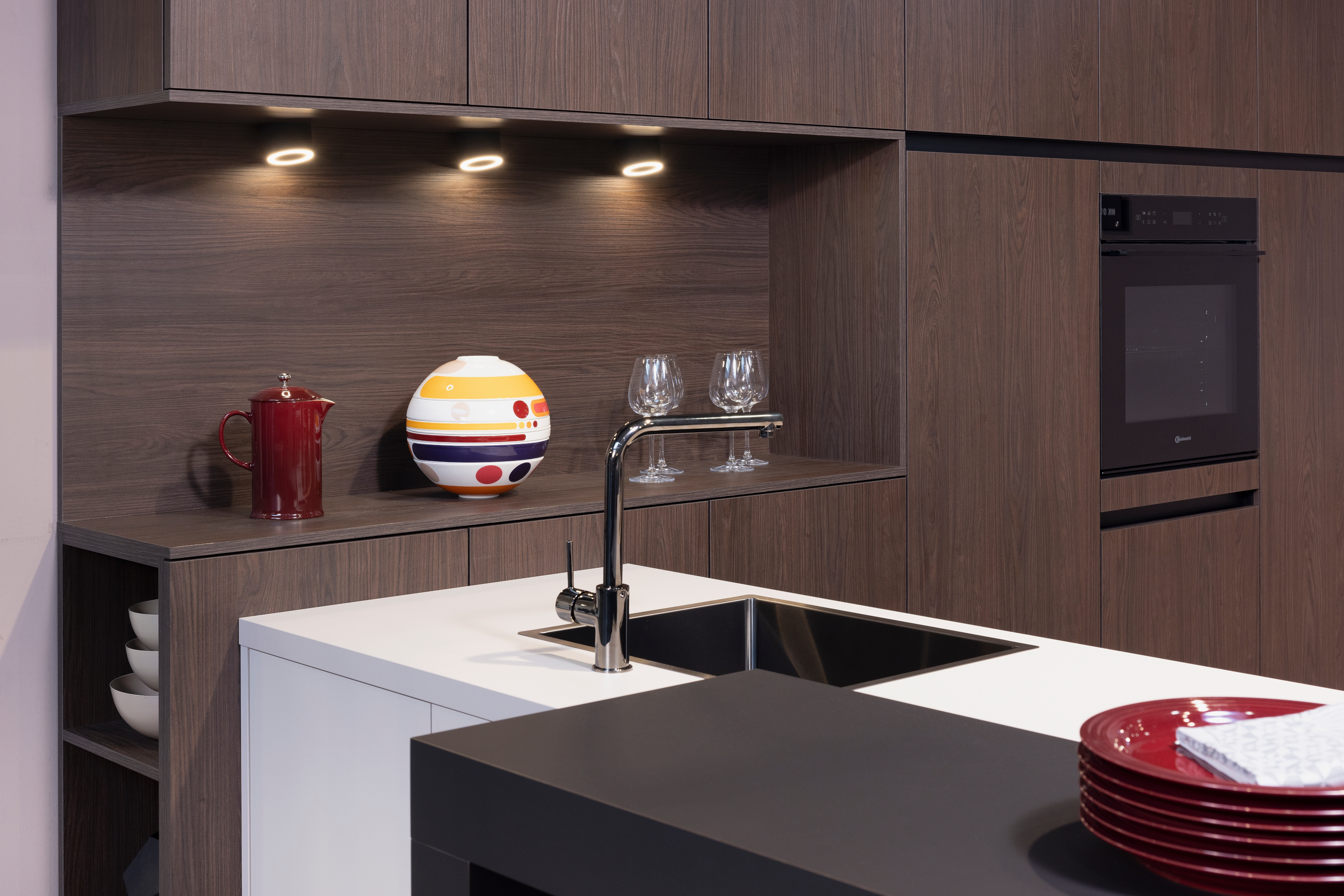 Moderne Küche mit dunklen Holzfronten, weißer Arbeitsplatte und roten Akzenten.