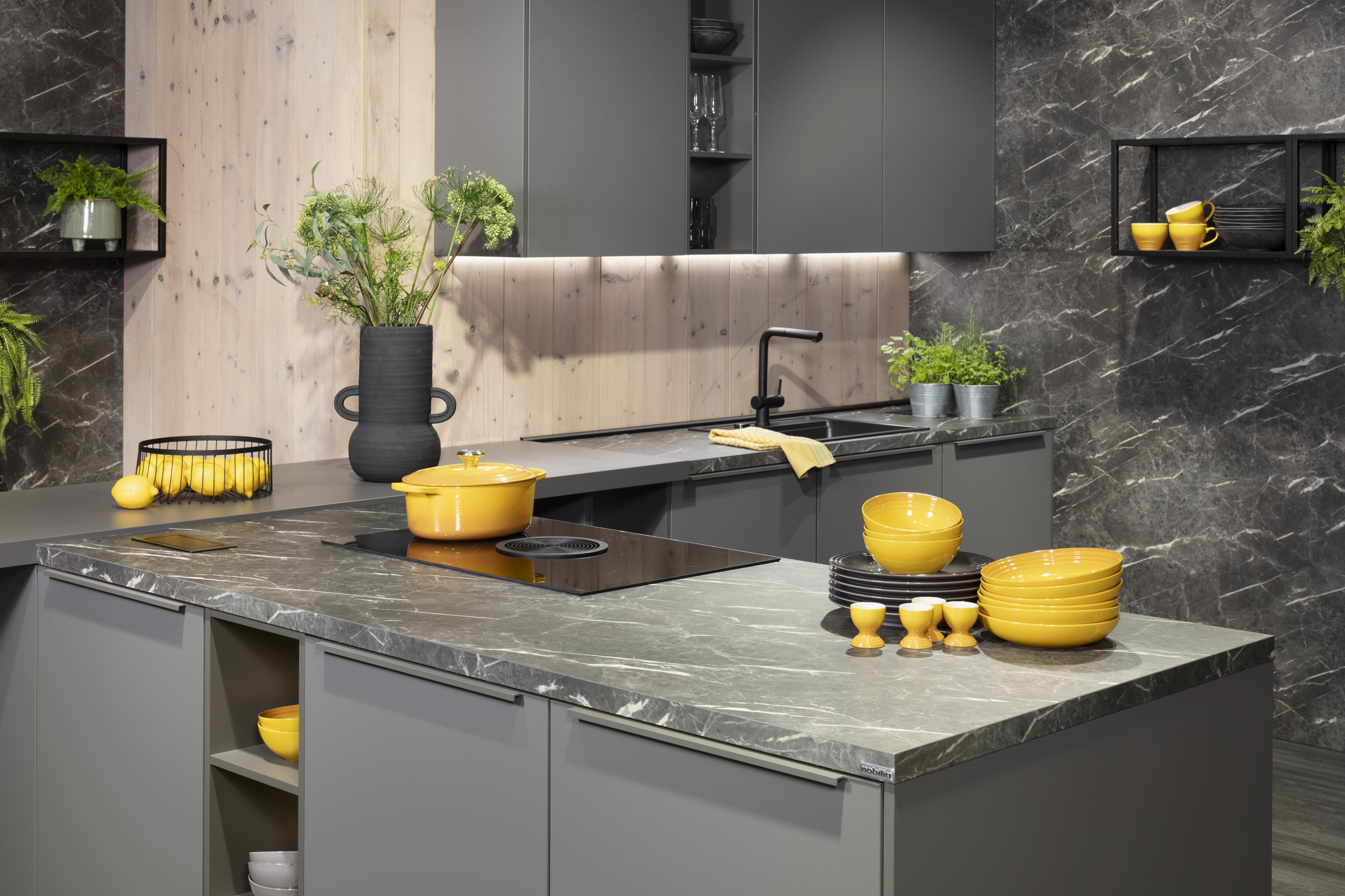 Moderne graue Küche mit gelben Töpfen und Schalen, frische Kräuter auf der Arbeitsplatte.