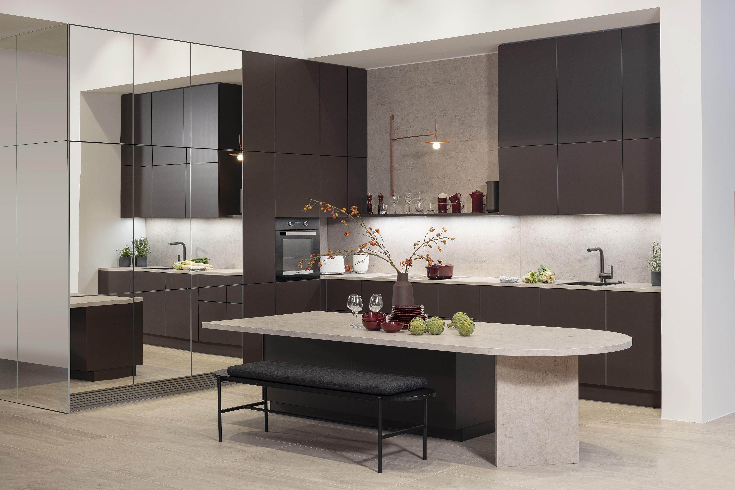 Moderne Küche mit dunklen Schränken, großem Tisch und Spiegelwand.