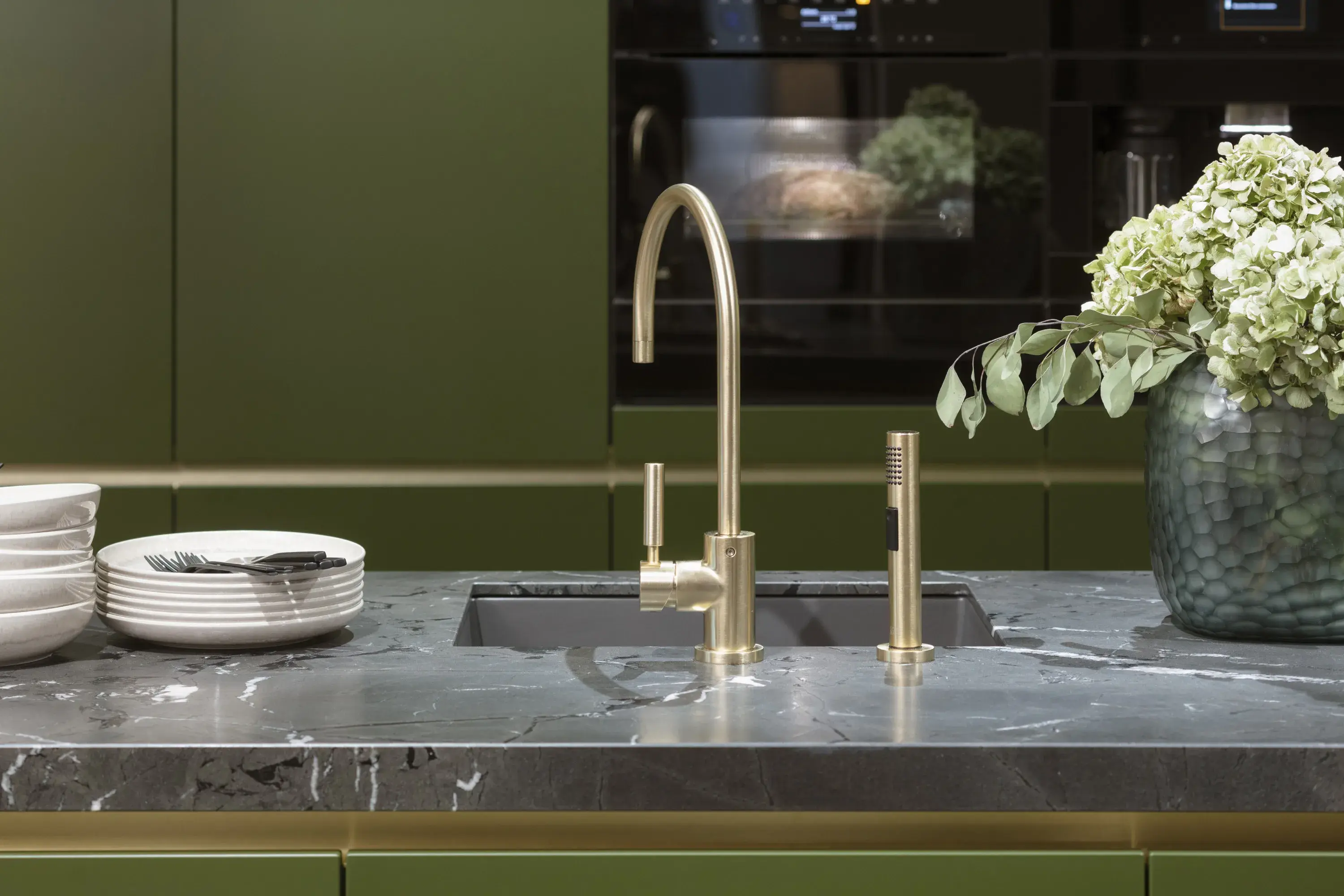 Moderne Küche mit Marmor-Arbeitsplatte, Messingarmatur und Vase mit weißen Blumen.